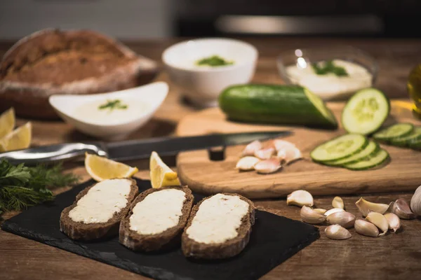 Enfoque selectivo de pan con salsa tzatziki e ingredientes frescos en mesa de madera - foto de stock