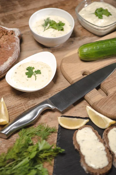 Tasty homemade tzatziki sauce with bread and greenery on wooden table — Stock Photo