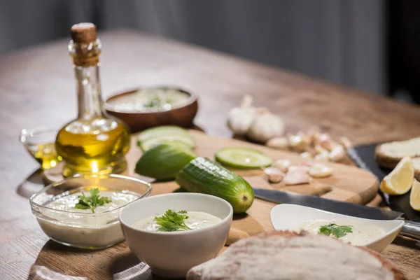 Delicious tzatziki sauce with ingredients and olive oil on wooden kitchen table — Stock Photo