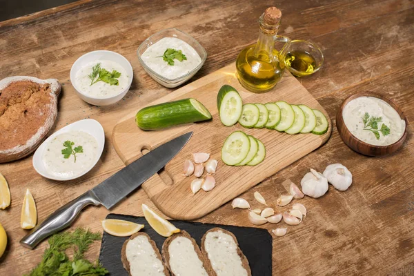 Fresh ingredients with olive oil and tzatziki sauce in bowls on wooden table — Stock Photo