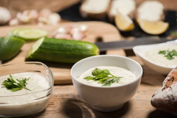 Selective focus of traditional greek tzatziki sauce with ingredients on wooden table — Stock Photo