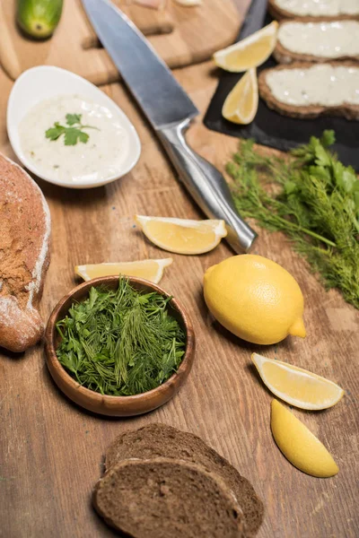 Bread, greenery and ingredients tor tzatziki sauce on wooden table — Stock Photo