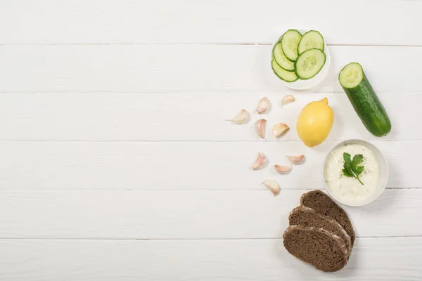 Top view of tzatziki sauce with organic ingredients and bread on white wooden background — Stock Photo