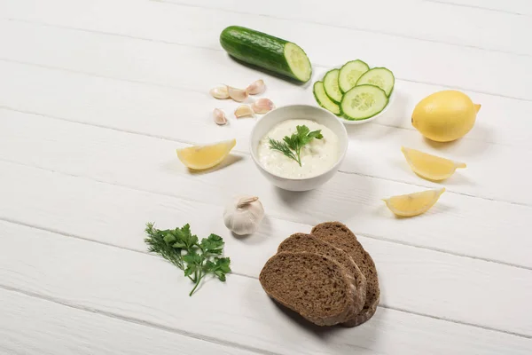 Delicious tzatziki sauce with fresh ingredients and bread on white wooden background — Stock Photo