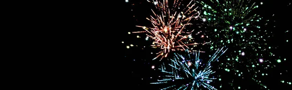 Panoramic shot of blue, green and orange festive fireworks in dark night sky, isolated on black — Stock Photo