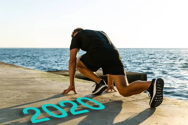 Young runner standing in start position on embankment near 2020 lettering — Stock Photo