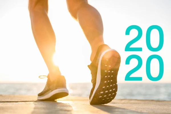 Vista recortada del corredor en zapatillas de deporte cerca de 2020 letras en el sol - foto de stock
