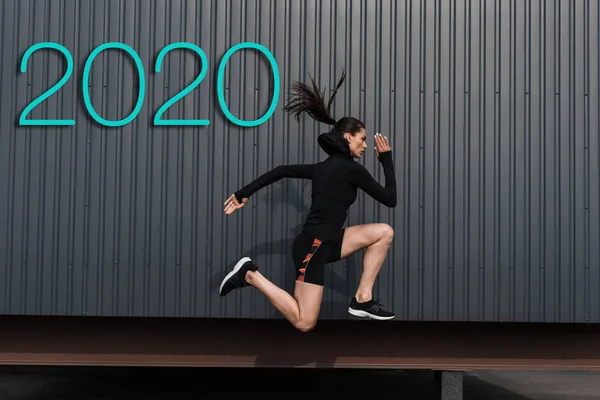 Side view of asian sportswoman running near wall with 2020 lettering — Stock Photo