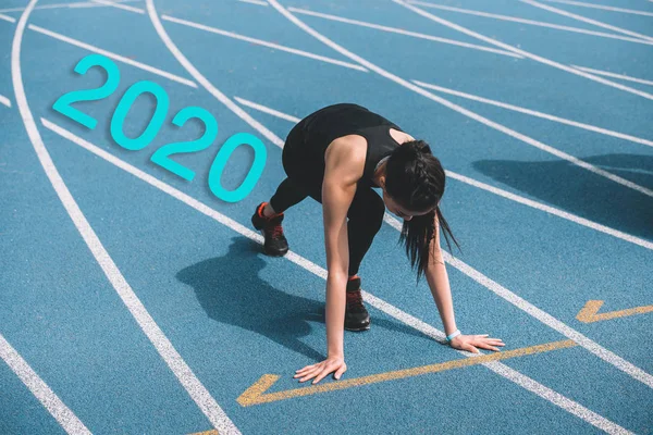 Молодая спортсменка, стоящая в начале позиционирования на беговой дорожке около 2020 года надпись — стоковое фото