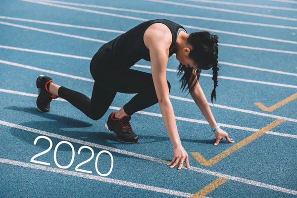 Young sportswoman standing in start positing on running track near 2020 lettering — Stock Photo