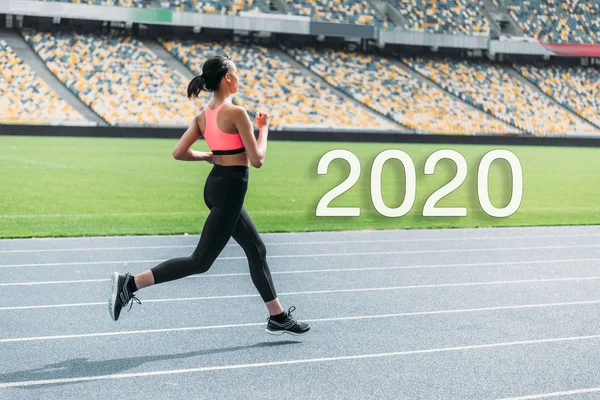 Jovem esportista afro-americana correndo no estádio perto de 2020 lettering — Fotografia de Stock