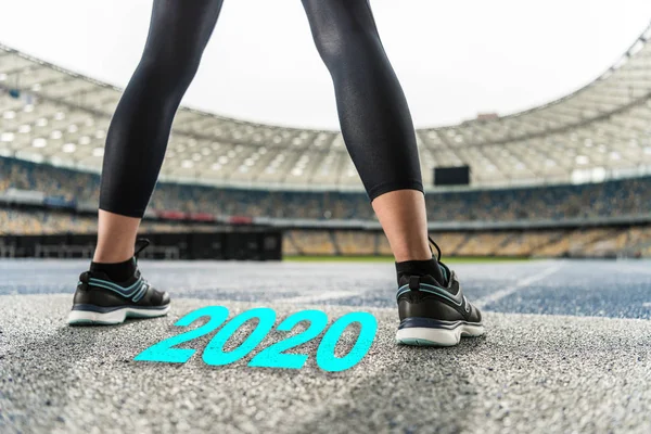 Vista cortada de esportista em pé na pista de corrida perto 2020 lettering — Fotografia de Stock