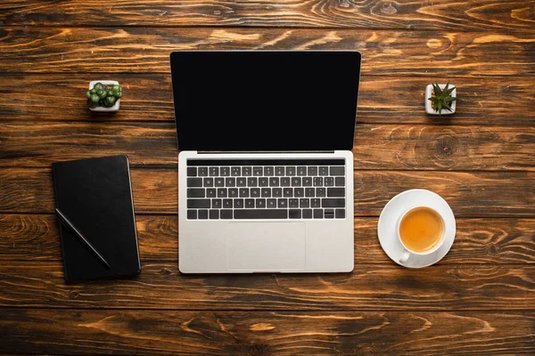 Вид зверху на ноутбук з порожнім екраном, чашкою кави, ноутбуком та горщиками на дерев'яному столі — стокове фото