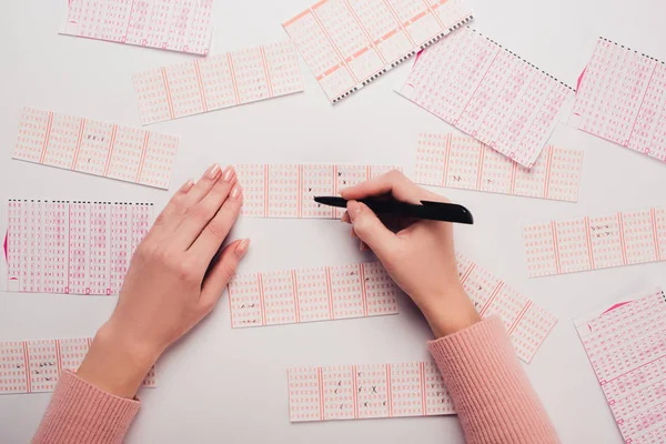 Vista parcial de la mujer marcando números en billetes de lotería en mesa blanca - foto de stock