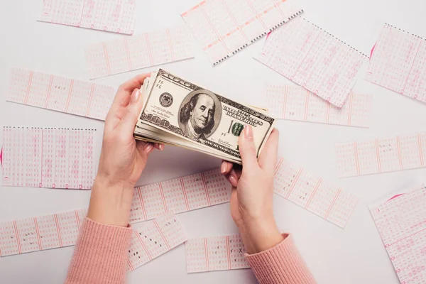 Vista cortada de mulher segurando notas de dólar perto de bilhetes de loteria espalhados na mesa branca — Fotografia de Stock