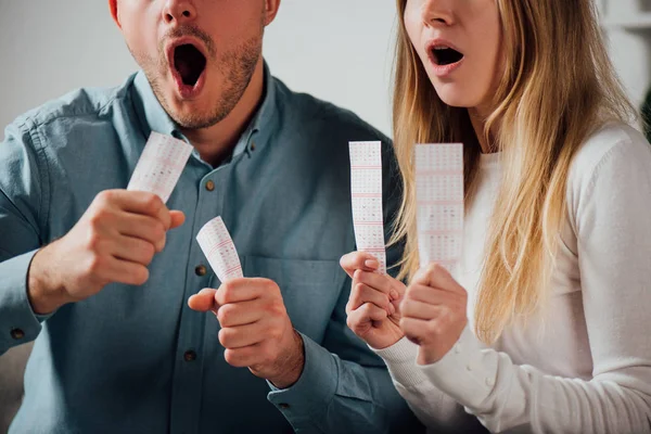 Vista recortada del hombre y la mujer impactados sosteniendo billetes de lotería - foto de stock