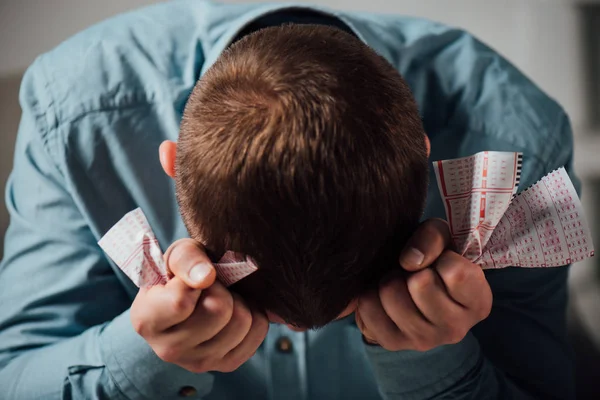 Unhappy man sitting with bowed head while holding crumpled lottery tickets — Stock Photo