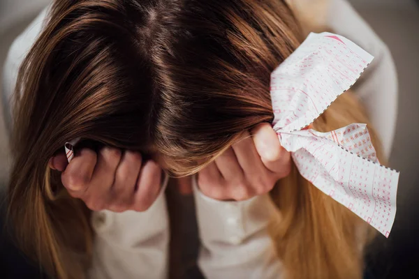 Unglückliche Frau sitzt mit gesenktem Kopf und hält zerknitterten Lottoschein in der Hand — Stockfoto