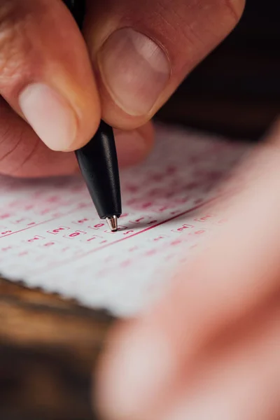 Selective focus of hand of gambler marking numbers in lottery ticket with pen — Stock Photo