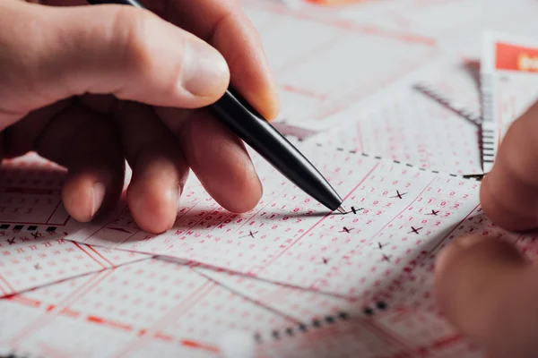 Ausgeschnittene Ansicht des Spielers, der Zahlen in Lottoscheinen mit Stift markiert — Stockfoto