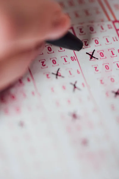 Selective focus of hand of gambler marking numbers in lottery ticket — Stock Photo