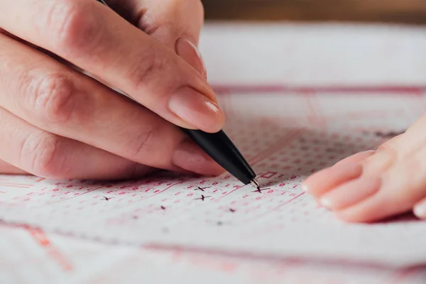 Ausgeschnittene Ansicht einer Frau, die mit Stift Zahlen in Lottoscheinen markiert — Stockfoto