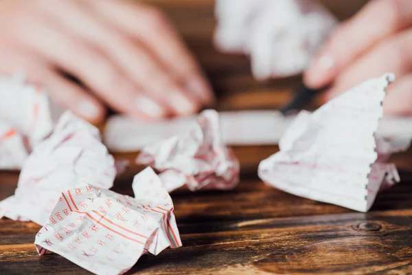 Selective focus of crumpled lottery tickets near gambler marking numbers in lottery card on wooden table — Stock Photo