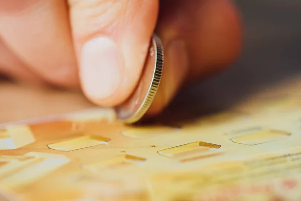 Close up view of silver coin in hand of gambler scratching lottery ticket — Stock Photo