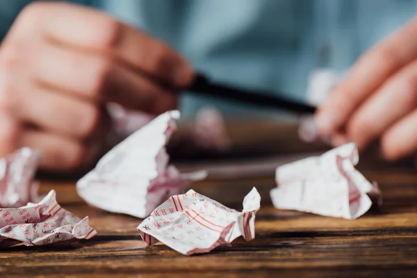 Cropped view of gambler holding pen near crumpled lottery tickets — Stock Photo