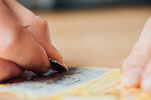 Selective focus of silver coin in hand of gambler scratching lottery ticket — Stock Photo