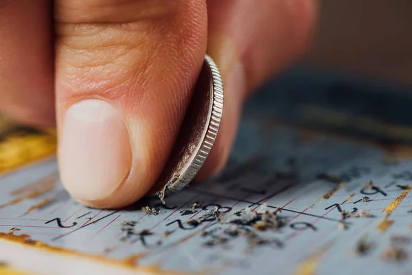 Nahaufnahme der Silbermünze in der Hand des Spielers, der Lotteriekarte zerkratzt — Stockfoto