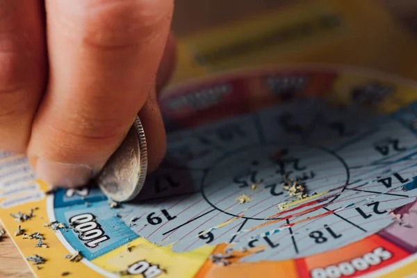 Vista ritagliata del giocatore d'azzardo graffiare biglietto della lotteria con moneta d'argento — Foto stock