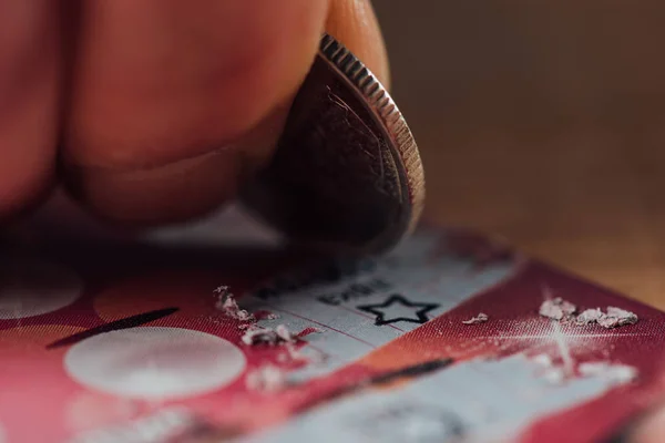 Vista de cerca de la moneda de plata en la mano del jugador rascando billete de lotería - foto de stock