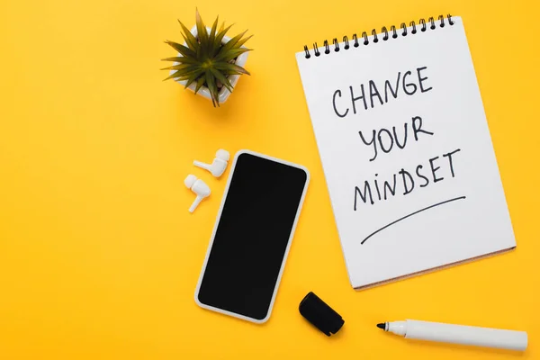 Notebook con cambiare la vostra iscrizione mentalità vicino smartphone, cuffie wireless, fiore in vaso e pennarello sul tavolo giallo — Foto stock