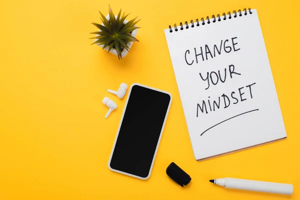 Bloc-notes avec changer votre état d'esprit inscription près du smartphone, casque sans fil, fleur en pot et feutre-pointe stylo sur table jaune — Photo de stock