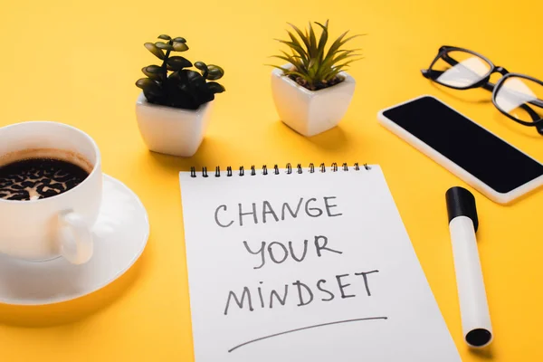 Carnet avec changement d'état d'esprit inscription près de tasse de café, plantes en pot, feutre stylo, smartphone et lunettes sur bureau jaune — Photo de stock