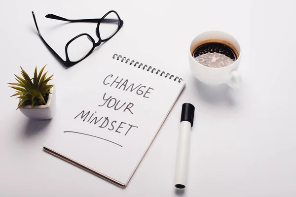 Notebook with change young mindset inscription, felt-tip pen, coffee cup, glasses and potted plant on white surface — Stock Photo