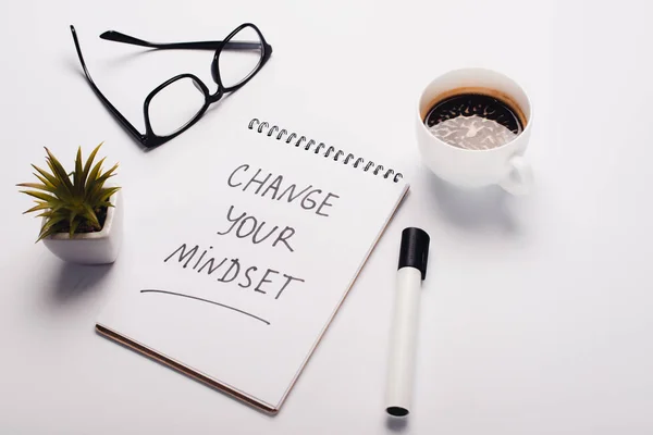 Libreta con inscripción de cambio de mentalidad joven, rotulador, taza de café, vasos y maceta en la superficie blanca — Stock Photo