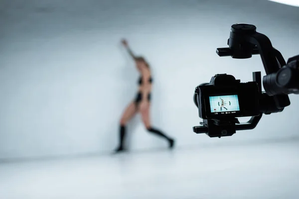 Selective focus of digital camera shooting girl in black outfit twerking near white brick wall — Stock Photo