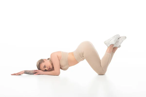 Side view of blonde girl in beige leggings twerking on floor isolated on white — Stock Photo