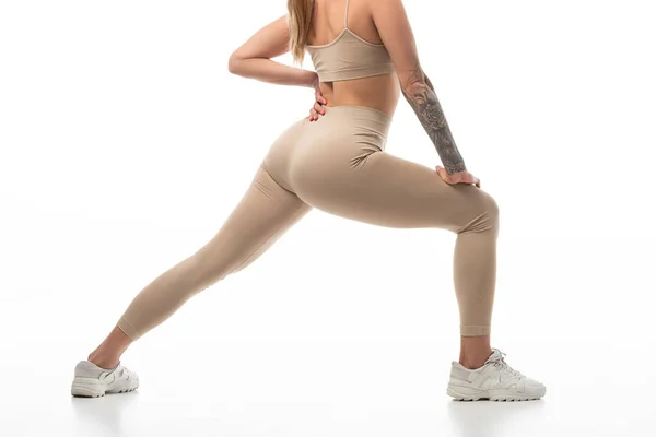 Corte vista de tatuado twerk dançarina em leggings bege posando isolado no branco — Fotografia de Stock