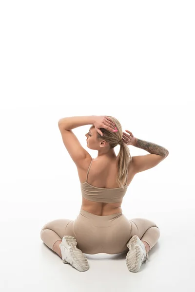 Rückansicht der blonden Twerk-Tänzerin in beigen Leggings, die isoliert auf weißem Boden sitzt — Stockfoto