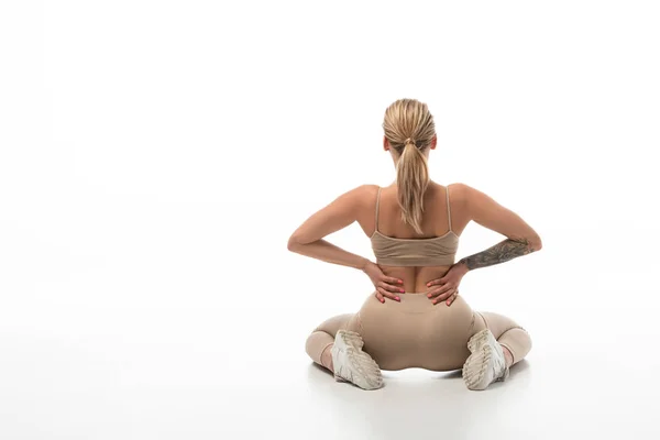 Rückansicht der blonden Twerk-Tänzerin in beigen Leggings, die isoliert auf weißem Boden sitzt — Stockfoto