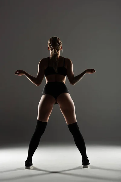 Rückansicht von sexy Mädchen im schwarzen Outfit, die im Schatten auf grauem Hintergrund twerking — Stockfoto