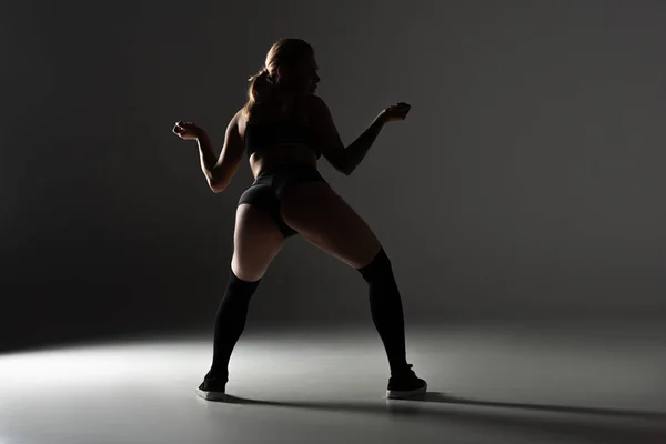 Back view of sexy girl in black outfit  twerking in shadow on grey background — Stock Photo