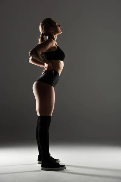 Side view of sexy girl in black outfit  twerking in shadow on grey background — Stock Photo