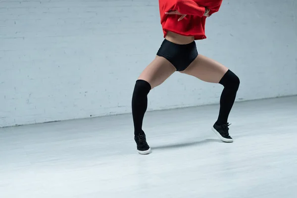 Vue recadrée de fille sexy en tenue noire et rouge twerking en studio — Photo de stock
