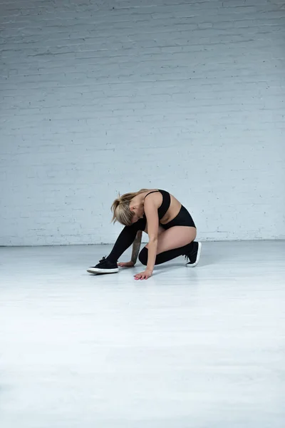 Tattooed sexy blonde girl in black outfit dancing in studio — Stock Photo