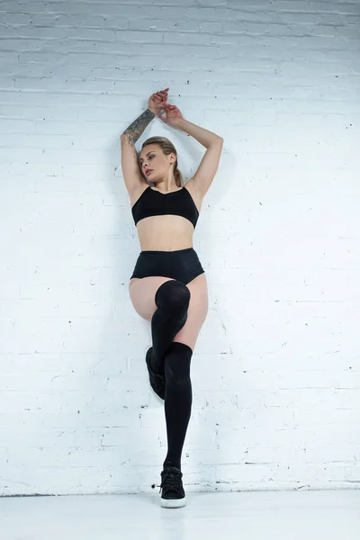 Tattooed sexy blonde girl in black outfit dancing near wall in studio — Stock Photo