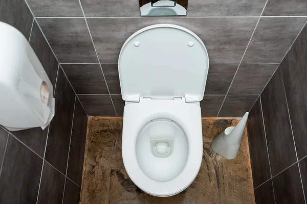 Керамическая чистая унитаз в современном туалете с серой плиткой и туалетной щеткой — стоковое фото